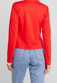 Haut rouge à manches longues avec une coupe ajustée, fabriqué en tissu lisse. Associé à un jean en denim bleu clair taille haute avec poches et détails de couture.