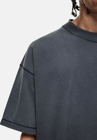 T-shirt oversize grigio scuro a maniche corte con scollo rotondo, caratterizzato da dettagli di cucitura visibili e una texture di tessuto morbido e liscio.