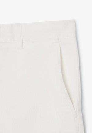 Primo piano di pantaloni bianchi che mostrano la cintura, le passanti per la cintura e la tasca laterale con dettagli di cuciture pulite.