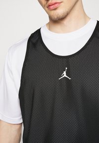 Svart mesh träningstopp med vitt Air Jordan-logotyp, lager på en vit t-shirt med kort ärm, med rund halsringning och perforerat tyg.