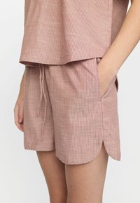 Bavlnený domáci set v mäkkej rezavej farbe s bielymi vertikálnymi pruhmi. Obsahuje voľný vrch a šortky so stehovaným lemom a bočnými vreckami.