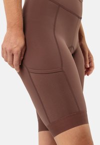 Bruine fietsbroek van rekbaar materiaal, met een gestructureerde zijzak en een gladde afwerking, met een aansluitend ontwerp en een lengte tot halverwege de dij.