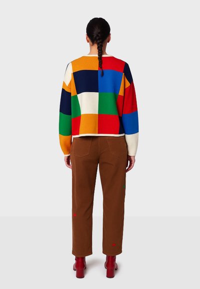 Kleurrijke gebreide trui met grote vlakken in rood, blauw, groen, geel en wit. Gecombineerd met een bruine broek en rode enkellaarzen.