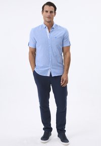 Niebieska koszula w paski z krótkim rękawem i kołnierzykiem zapinanym na guziki, w połączeniu z granatowymi spodniami typu tapered i ciemnymi sneakersami. Prosty, casualowy design.