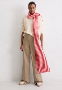 Écharpe à rayures rouges et blanches pos�ée sur un pull clair et un pantalon large beige. Tissu doux et décontracté avec une coupe ample.