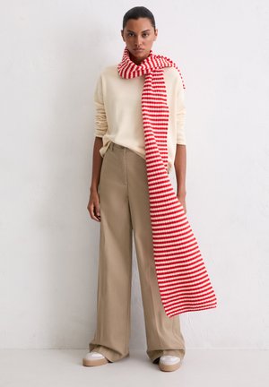 Rood-wit gestreepte sjaal gedrapeerd over een lichtgekleurde trui en beige wijde broek. Casual, zachte stof met een ontspannen pasvorm.