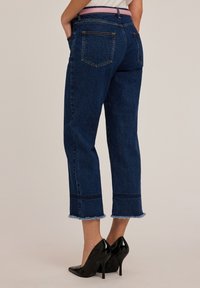 Donkerblauwe denim cropped jeans met een rafelige zoom, twee achterzakken en contrasterende stiksels. Gepaard met zwarte hoge hakken.