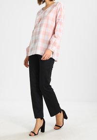 Blusa a cuadros en rosa claro y blanco con mangas largas, combinada con pantalones negros ajustados y sandalias de tacón alto. Diseño simple y casual.