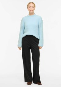 Hele sinine tekstuuriga kudumist kvaliteediga kampsun, millel on pikkade varrukatega ja ümmargune kaelus, kantud koos mustade, laia lõikega pükstega ja pruunide jalanõudega.