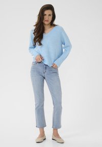 Un pull en maille bleu clair avec un col en V, associé à un jean délavé et des ballerines beiges. Le pull est de coupe décontractée et possède un ourlet côtelé.