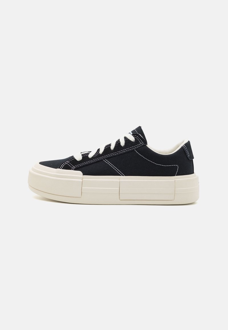 Black canvas sneakers with white stitching, thick cream sole, round toe, and white laces. Minimalist design, no visible logos or patterns.