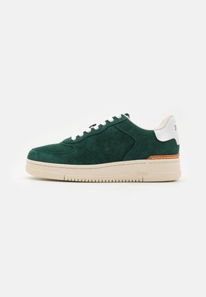 Green suede sneaker with white leather accents, flat white laces, and a cream rubber sole. Features subtle stitching and logo detail.