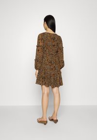 Vestido mini marrón con un patrón, mangas largas, volantes en capas y ajuste ceñido. Se combina con zuecos abiertos beige, con tacón plano.