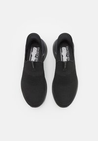 Fekete elasztikus slip-on sportcipők, kötött felső résszel, texturált mintázattal és gumi talppal, párnázott sarokkal a kényelem érdekében.