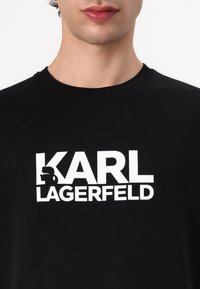 T-shirt en coton noir avec un logo "KARL LAGERFELD" en blanc audacieux et un design de silhouette, col rond et manches courtes.