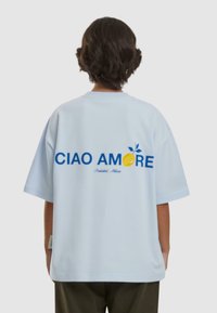 Lyseblå oversized t-skjorte med en gul sitrongrafikk og teksten "CIAO AMORE" i blått på baksiden. Laget av myk stoff.