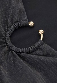 Black garment detail featuring a gathered edge, metallic gold hardware accents, and a textured fabric with subtle sheen.