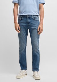 Světle modrá košile s krátkým rukávem, modré džíny z denimu, rovný střih, vybledlý vzhled, kontrastní stehy, doplněné o béžové tenisky.