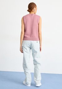 Sleeveless, pastel pink knit sweater with a crew neck and ribbed hem, paired with light blue cargo pants and white sneakers.