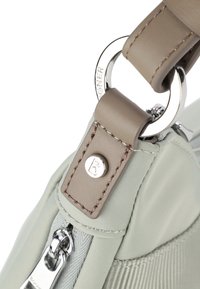 Dettaglio di una borsa a tracolla in nylon verde chiaro con una tracolla in pelle taupe e un anello in argento con accento del logo, chiusura con zip e tessuto testurizzato.