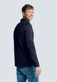 Marineblauwe polo met lange mouwen en kraag, gedragen met blauwe jeans. Heeft een soepele textuur en een getailleerd ontwerp.