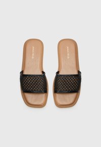 Svarte vevde sandaletter med bred stropp, glatt tan fotbed og firkantet tådesign. Teksturerte overflatedetaljer forbedrer grep.