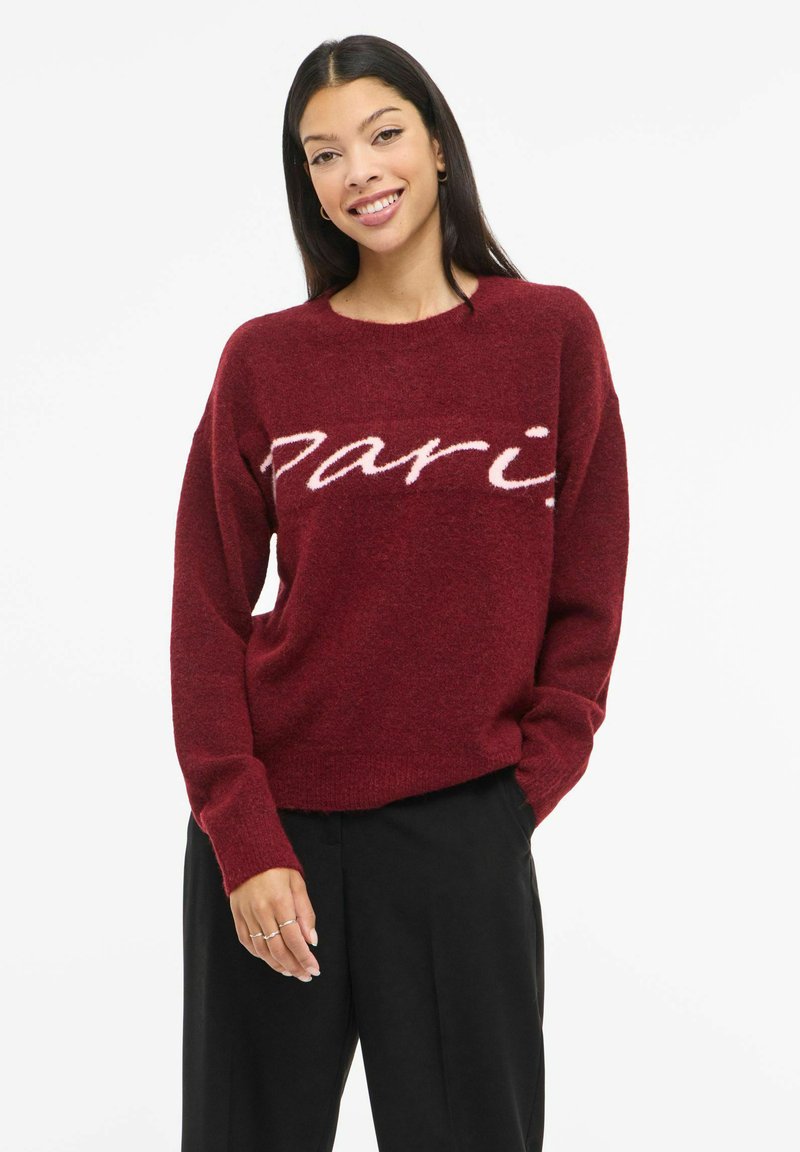 Bordeauxrode gebreide trui met een losse pasvorm, voorzien van een zachte, pluizige textuur en het woord "Paris" in lichtroze aan de voorkant.