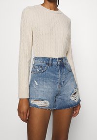 Maglione crema a maglia grossa con collo rotondo e maniche lunghe abbinato a pantaloncini di jeans blu a vita alta con dettagli strappati.