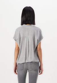 Gestreifte kurzärmlige Bluse in Grau und Weiß, mit einer lockeren, lässigen Passform und einem gefalteten Rücken. Kombiniert mit enganliegenden grauen Jeans.