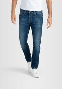 Dunkelblaue Denim-Jeans mit Slim-Fit, fünf Taschen und dezenten Auswaschungen. Kombiniert mit weißen Sneakers, die eine glatte Textur aufweisen.