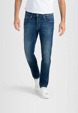 Dark blue denim jeans with a slim fit, five-pocket design, and subtle fading. Paired with white sneakers, featuring a smooth texture.
