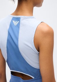 Κοντινό σε πάνω μέρος της πλάτης ενός ατόμου που φοράει αμάνικο αθλητικό τοπ μπλε και ανοιχτό γκρι με διάτρητο ύφασμα και λευκό λογότυπο κοντά στη γραμμή του λαιμού.