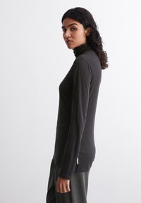 Tumši pelēks ilgs piedurknes turtlenecks krekls no mīksta auduma, šaura piegriezuma dizains, ar augstu apkakli un sānu šķēlumu apakšmalā.