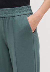 Teal joggers med elastisk midja och sidofickor, tillverkade av mjukt tyg med en slät yta och rak byxdesign.