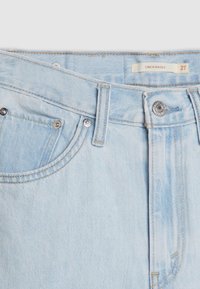 Light blue denim jeans with a cinched baggy design, featuring silver-tone button hardware, contrasting stitching, and a front pocket.