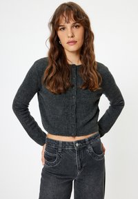 Cardigan cropped grigio scuro con maniche lunghe, scollatura rotonda e chiusura con bottoni. Tessuto morbido con un sottile motivo a maglia.