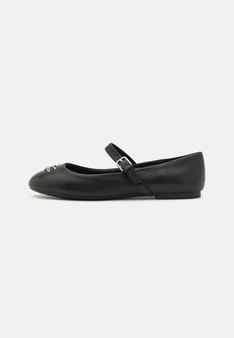 Black flat shoe with a rounded toe, a soft leather exterior, a buckled ankle strap, and decorative metallic detailing on the toe.