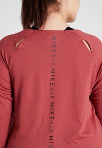 Rode textuur sportshirt met uitsparingen op de schouders. Heeft een verticale "NIKE AIR"-logo in zwart langs de achternaad.