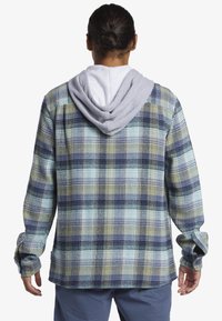 Karierter Flanellhemd mit grauem Kapuzen, das Blau-, Gelb- und Grüntöne aufweist. Das Material hat einen strukturierten Stoff mit langen Ärmeln und Knopfbündchen.