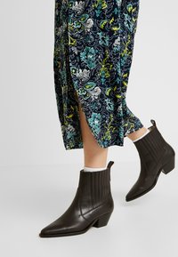 Bruna läderankelstövlar med spetsig tå och låg, kraftig klack. Har vertikal söm och dragflik. Stylar med en blommönstrad kjol.