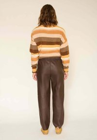 Pull rayé en laine orange, marron et beige, associé à un pantalon en cuir marron. Il présente une coupe décontractée avec une taille élastique.