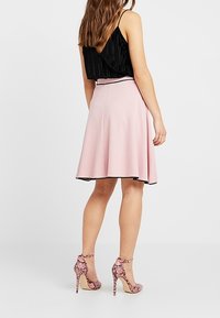 Vaaleanpunainen A-linjainen hame mustalla reunuksella, yhdistettynä mustaan laskostettuun puseroon ja vaaleanpunaisiin käärmeennahkakuosisarviin korkokenkiin. Takaviistosta otettu kuva asusta.