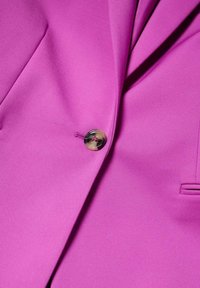 Veste magenta vif avec revers cranté, une seule boutonnière sombre et une poche passepoilée sur le côté droit.