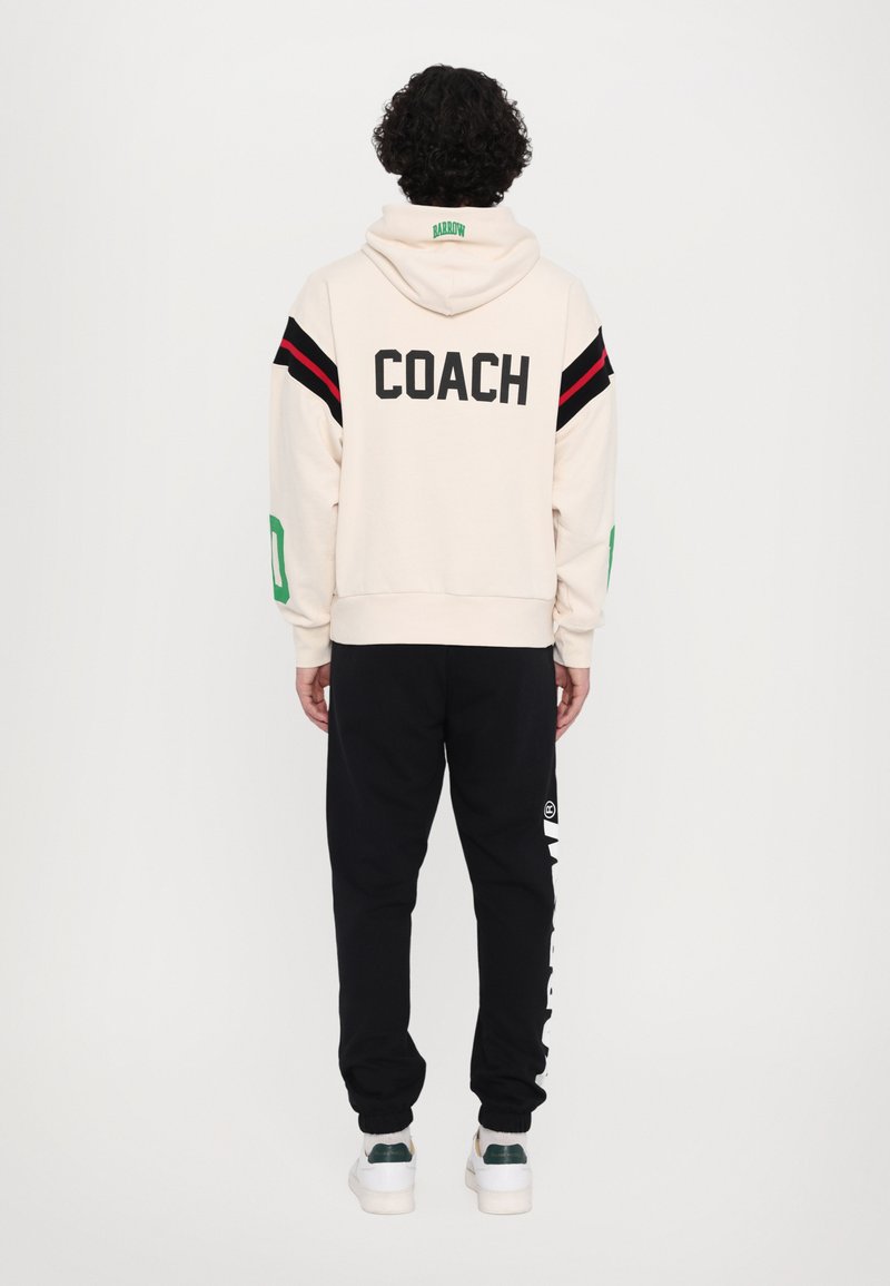 Cream hoodie with "COACH" printed on the back; features red and black stripes on sleeves. Pair of black joggers with white side print.
