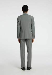 Abito grigio su misura con rever a punta, apertura singola e pantaloni slim fit. Realizzato in tessuto leggero e morbido; abbinato a scarpe nere.