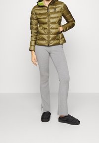 Chaqueta acolchada color verde oliva con diseño acolchado horizontal, cierre de cremallera y capucha. Pantalones grises de canalé y zapatos negros tipo slip-on completan el conjunto.