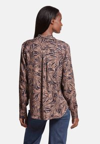 Langslavende blouse in bruin en marineblauw met een bladenpatroon, met een knoopsluiting aan de achterkant en een relaxte pasvorm. Gemaakt van gladde stof met een zachte textuur.