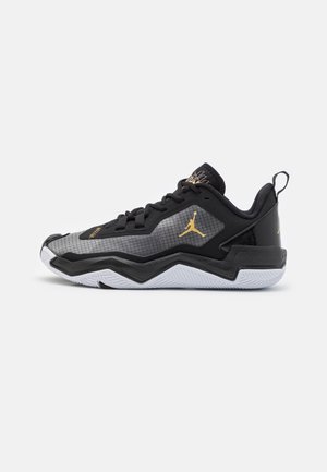 Zapatilla de baloncesto baja negra y gris con logo Jumpman dorado, suela blanca en zigzag, cierre de cordones en la parte delantera y cuello acolchado con lengüeta para tirar.