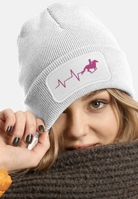 White knitted beanie featuring a pink graphic design of a horse and heartbeat. Soft texture and snug fit, with a wide cuff.