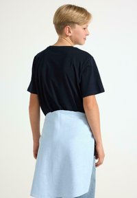 Sort t-shirt med korte ærmer, parret med et lyseblåt forklæde, set fra ryggen. Forklædet er knælængde og let tekstureret.